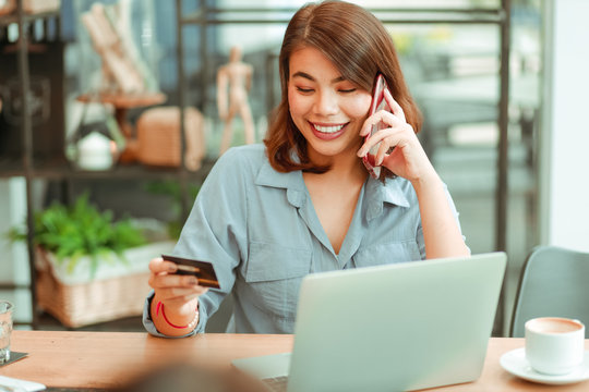 Asian Woman Using Mobile Phone With Credit Card And Laptop Computer For Shopping Online Payment In Coffee Shop Cafe With Freinds