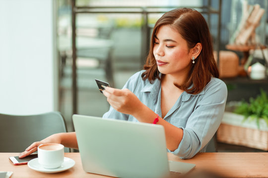 Asian Woman Using Mobile Phone With Credit Card And Laptop Computer For Shopping Online Payment In Coffee Shop Cafe With Freinds