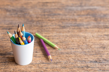 colorful colored pencil in a white cup on wooden background  and copy space