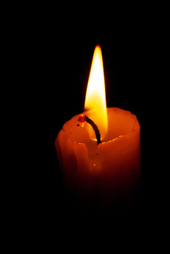A stearin candle burning in total darkness as the only source of light