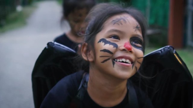 Asian little girls with a painted face is walking along the streets of the village to celebrating in halloween. The children in demon costumes is spell enchant so enjoyment in halloween. Slow motion