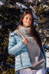 Portrait of a young beautiful brunette woman with blue eyes and freckles on face in winter snowy mountain landscape. Beautiful girl in the winter outdoors.