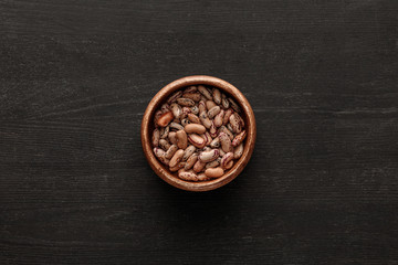 top view of brown bowl with raw beans on dark wooden surface with copy space