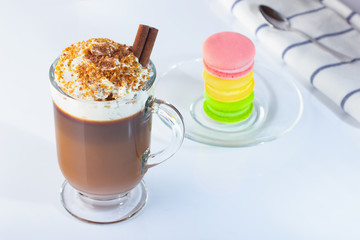 Cappuccino in a glass Irish glass, cinnamon stick, ground nut and chocolate chips. Glass plate, macaron cakes in three colors. The photo.
