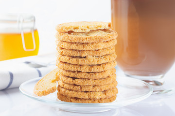 A stack of oatmeal cookies in a glass plate. Coffee in an Irish coffee glass, orange jam in a jar with a yoke. Linen napkin with a spoon for coffee. The photo.