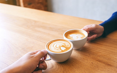 Close up image of a man and a woman clinking two coffee mugs on wooden table in cafe