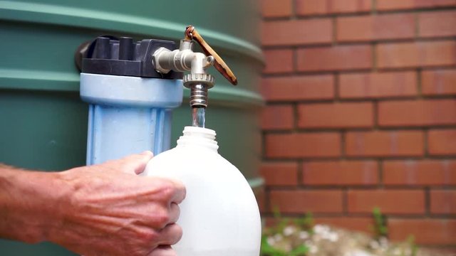 Male caucasian hands fill plastic container from water tank, close up
