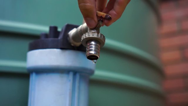 Dripping spigot on outdoor water tank turned off by male hand, close up