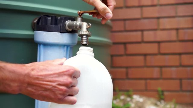 Slow mo, man fills plastic bottle directly from rain water tank, close up