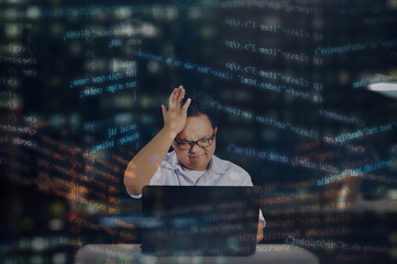 Young male programmer with glasses getting stressed out while coding for an HTML website or for web development. Shot behind office window at night with HTML codes surrounding the programmer. 