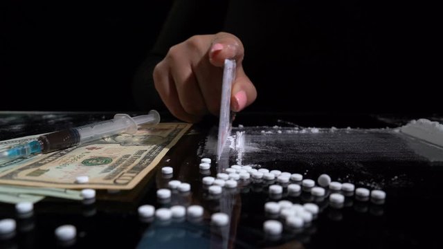 White cocaine powder on a table with dollar bills and a syringe
