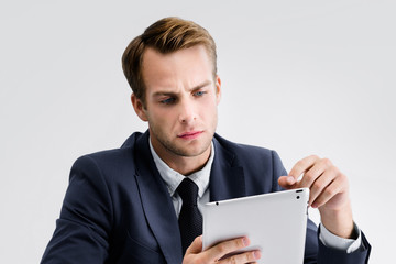 Young serious businessman in black confident style suit working with tablet computer at office. Success in business, job and education concept shot.