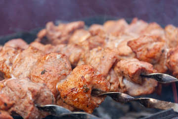 skewers of meat with smoke is cooking on the coals