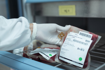 Selective focus scientist hand holding red blood bag in storage blood refrigerator at blood bank...