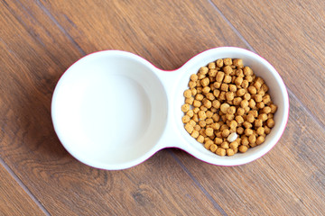 .double bowl of cat food with multivitamins without water on the wooden floor