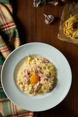 Fresh homemade italian Carbonara pasta with raw yolk, parmesan, white sauce, bacon in white bowl on wooden background.