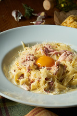Fresh homemade italian Carbonara pasta with raw yolk, parmesan, white sauce, bacon in white bowl on wooden background.