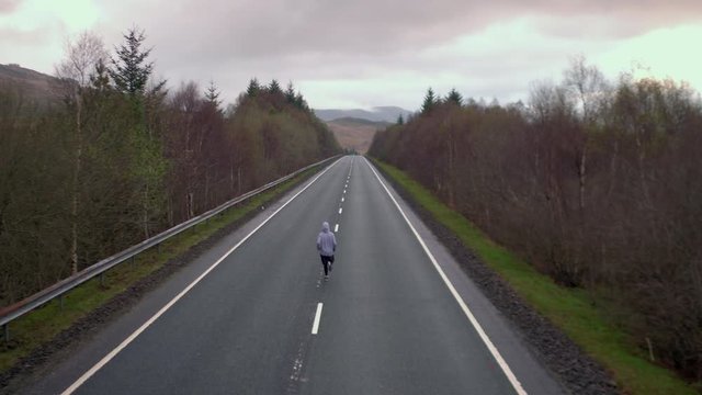 4K Man jogging on a road through the  Scottish Highlands in the evening. A runner travelling through a summer tourist landscape with trees against the rural Scotland countryside.