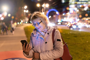 A woman with a mobile phone in her hand is walking through the night city.