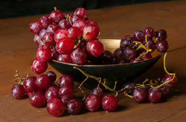 Still life, grapes on a golden bowl on a rustic wooden table 