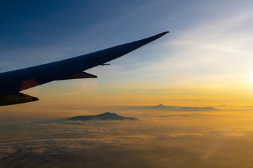 Sunset sky and view on mountains in clouds from the airplane window
