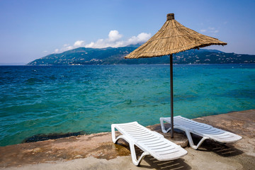 Straw umbrella and a pair of sunbeds on the beach of Saranda, Albania