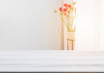 White wood table top with flower pot in living room background with morning light from window