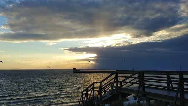 View on Gulf of Gdansk on Baltic Sea from Pier with sun under clouds in Hel, Poland, Europe at sunset