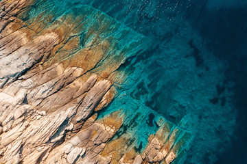 Aerial view of a slide turn from a drone on the view of calm turquoise sea water and rocks from molten lava. Pattern of sea surface and rocky shore. Thracian Sea, Greece. Rocky coast of the peninsula