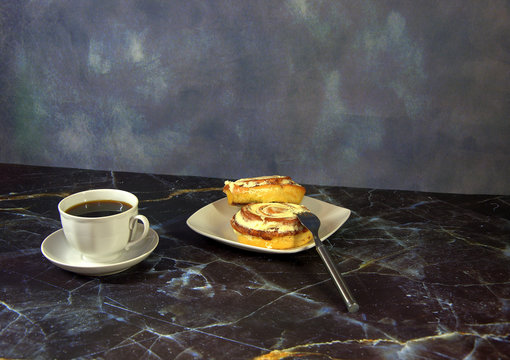 A cup of black coffee on a saucer and bwe cinnamon rolls on a plate, next to a fork.