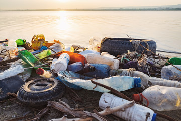 Obraz premium Spilled garbage on the beach of the big city. Empty used dirty plastic bottles. Dirty sea sandy shore the Black Sea. Environmental pollution. Ecological problem. Bokeh moving waves in the background