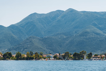 Fototapeta premium Yacht at small seaside resort town in the mountains of Greece on the island on the coastline in the open sea. Blue sea overlooking the coast of the island. Small waves Tourism
