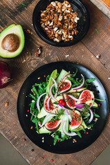 salad on a black matte plate: arugula, figs, avocado, red onions, cucumbers, walnuts, viburnum, thyme, spices