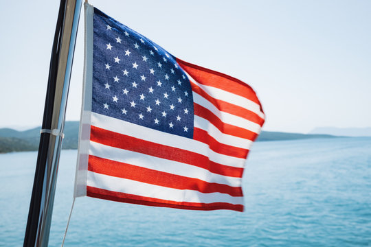 American flag fluttering in the wind on a sailing yacht sailing on the blue sea against the blue sky, the horizon with the shores of the islands.