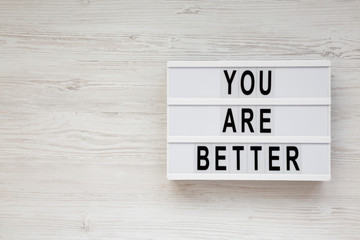 'You are better' words on a lightbox on a white wooden background, top view. Overhead, from above. Flat lay. Copy space.