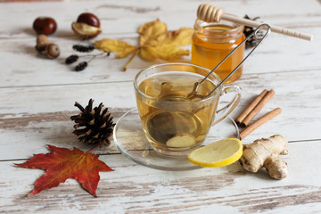 A cup of autumn tea with ginger, lemon and cinnamon on wooden background with autumn leaves decoration.