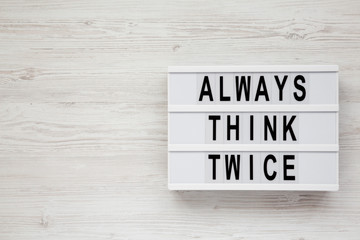 'Always think twice' words on a lightbox on a white wooden background, top view. Overhead, from above, flat lay. Copy space.