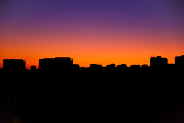 Bright orange sunset over the city in the evening. Bright lights of high-rise buildings of urban buildings. Silhouette of construction city crane of building under construction