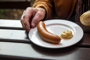 Mann isst Bockwurst mit Senf und Brötchen im Biergarten