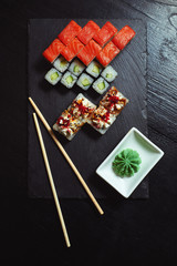 Fresh sushi rolls on black slate and dark wood, top view
