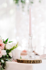 A tall thin paraffin candle of gentle pink color in a glass candlestick.