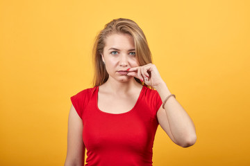 young blonde girl in red t-shirt over isolated orange background shows emotions