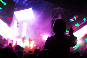 Child has fun on her parents' shoulders keeping hands with them at an outdoor rock music concert