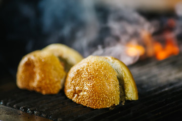 Making and grilling hamburger buns with sesame on coal grill. Preparing roasted food on barbecue BBQ grill in outdoor fireplace and u-shape fire grid. Last step of making delicious burgers. 