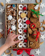 a woman's hand holding a cookie above an open box full of various cookies