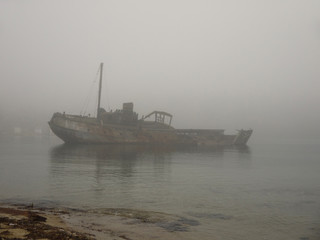 An old wooden shipwreck whaling boat abandoned stand on beach on foggy morning 
