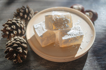 Delicious white turkish delight on wooden dish sprinkled with icing sugar like snow. Oriental pieces of flavoured sweets next to pine cones and chestnut nuts. Winter Christmas dessert in the sunshine