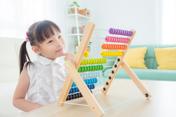 Little asian girl playing colorful wooden abacus in living room at home.