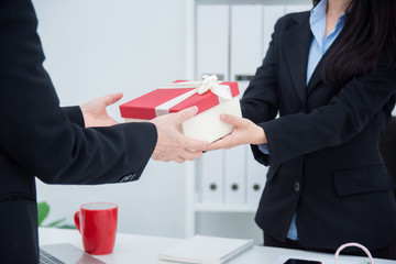 Hands of businesswoman giving christmas gift to her boss in office.