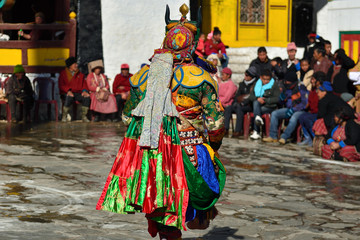Tawang, Arunachal Pradesh, India, Buddhist monk dancing in disguise for the Torgya  festival, in the background there are monastery and many gathered viewers.